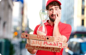 Livreur en uniforme rouge tenant des boîtes à pizza et un sablier, l'air stressé, en milieu urbain