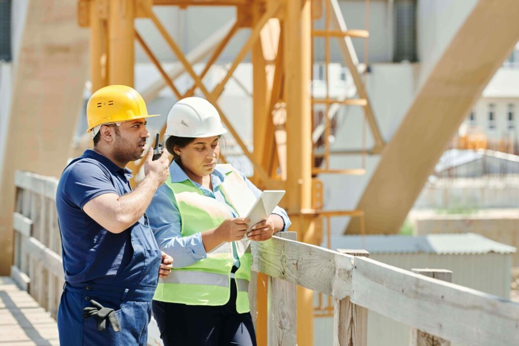 Deux professionnels équipés de casques de sécurité utilisent une radio et une tablette sur un chantier.