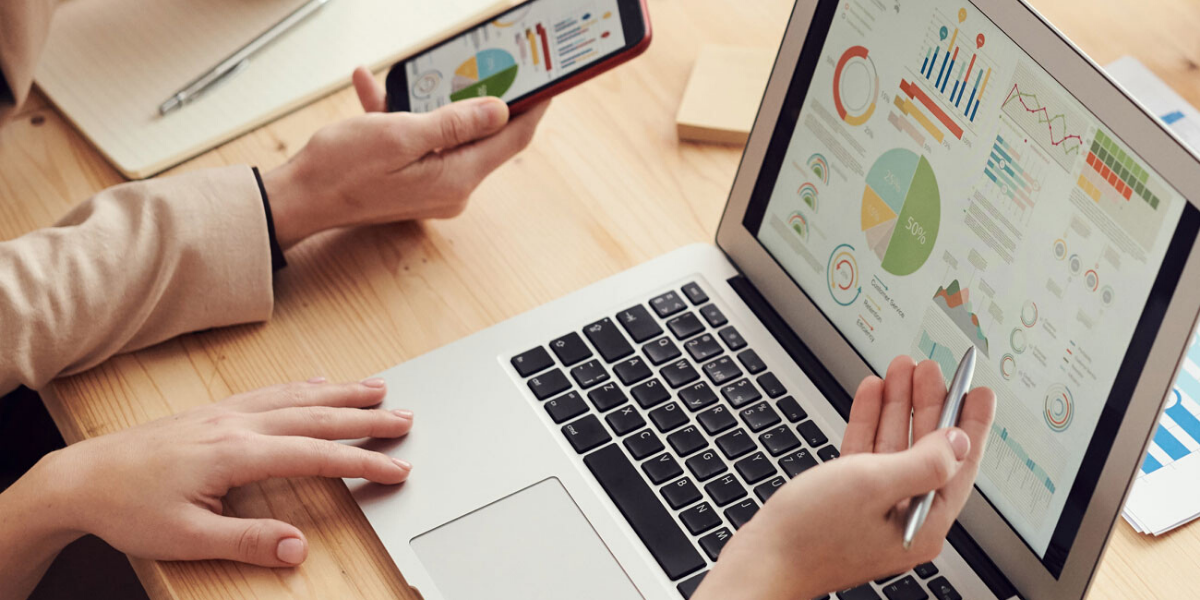 Image de deux personnes utilisant un ordinateur portable et un smartphone pour analyser des graphiques et des données, illustrant un logiciel de rapport de maintenance.
