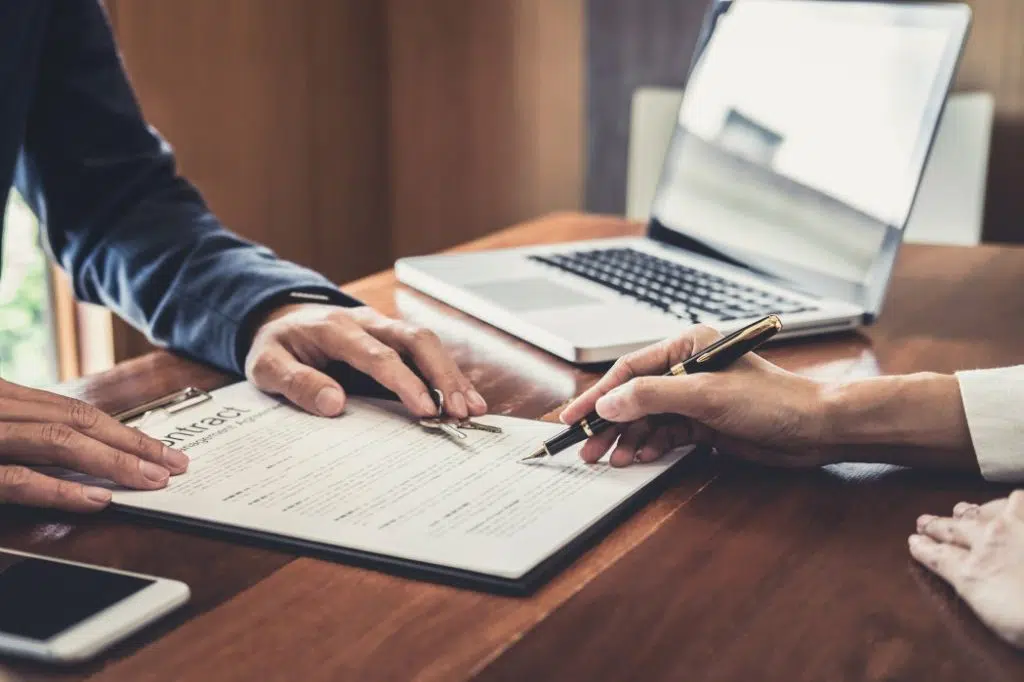 Image de deux personnes assises à une table en train de signer un contrat de gestion, avec un ordinateur portable ouvert à côté d'eux.
