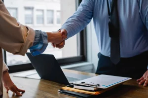 Image de deux professionnels se serrent la main, finalisant un accord dans le cadre d'un service de gestion de contrat, avec des documents et un ordinateur portable sur la table