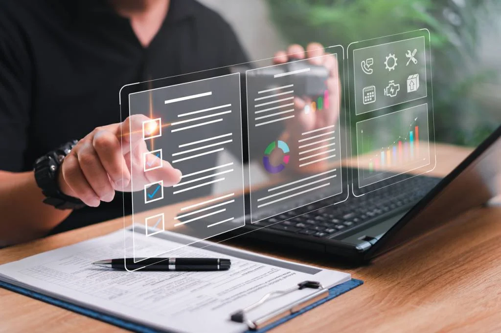 Image d'une personne interagissant avec une interface numérique holographique affichant des graphiques et des icônes, avec un ordinateur portable et des documents sur le bureau, illustrant un logiciel de planification de maintenance.