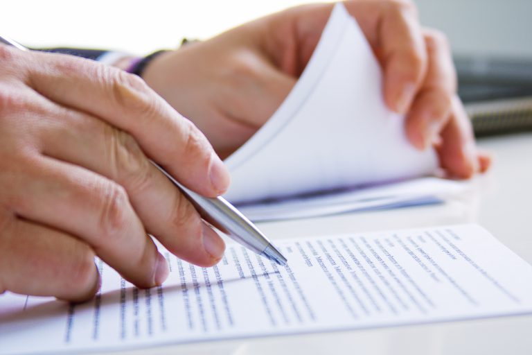 Mains tenant un stylo et feuilletant un document imprimé lors d'une relecture