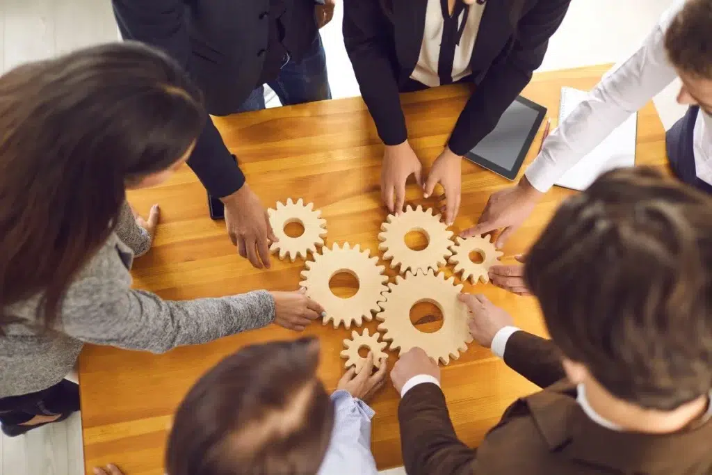 Équipe de professionnels assemblant des engrenages en bois autour d'une table, symbolisant la coordination et la gestion des interventions terrain