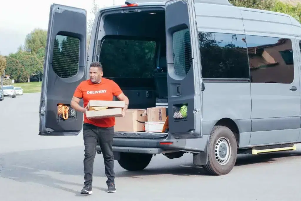 Livreur en t-shirt rouge "Delivery" déchargeant des colis depuis l'arrière d'un fourgon gris