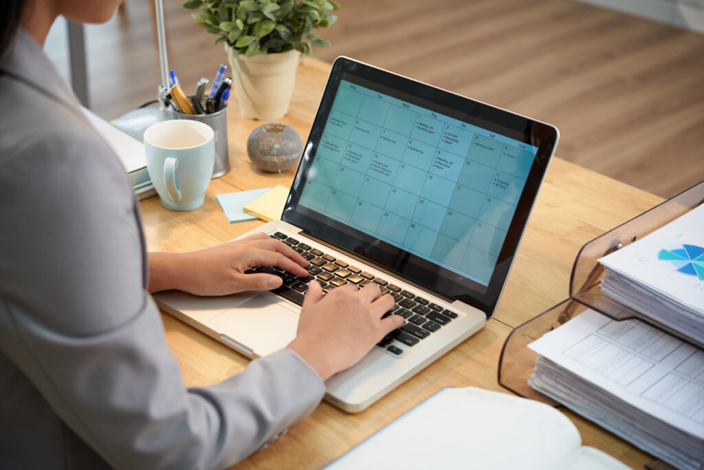 unrecognizable businesswoman sitting desk with laptop looking calendar scaled