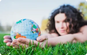 Femme aux cheveux bouclés allongée dans l'herbe tenant délicatement un petit globe terrestre coloré