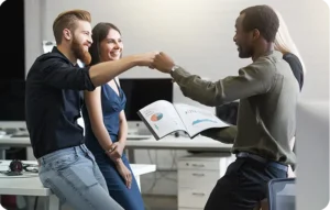 Trois collègues souriants faisant un fist bump pour célébrer un succès, l'un tenant un rapport avec graphiques