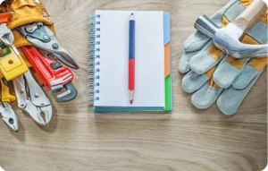 Outils de travail indispensables pour techniciens itinérants disposés sur une table en bois avec un carnet de notes au centre.