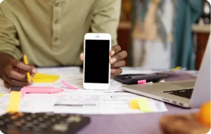 Commercial tenant un smartphone écran noir devant un bureau encombré de documents, post-its et ordinateur portable