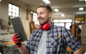 Technicien souriant en atelier avec casque antibruit et gants de protection consultant une tablette numérique