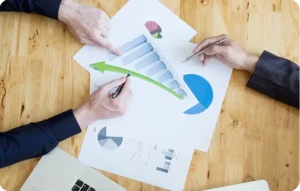 Vue plongeante sur deux professionnels pointant des graphiques en barres et circulaires avec une flèche de croissance verte sur des rapports imprimés