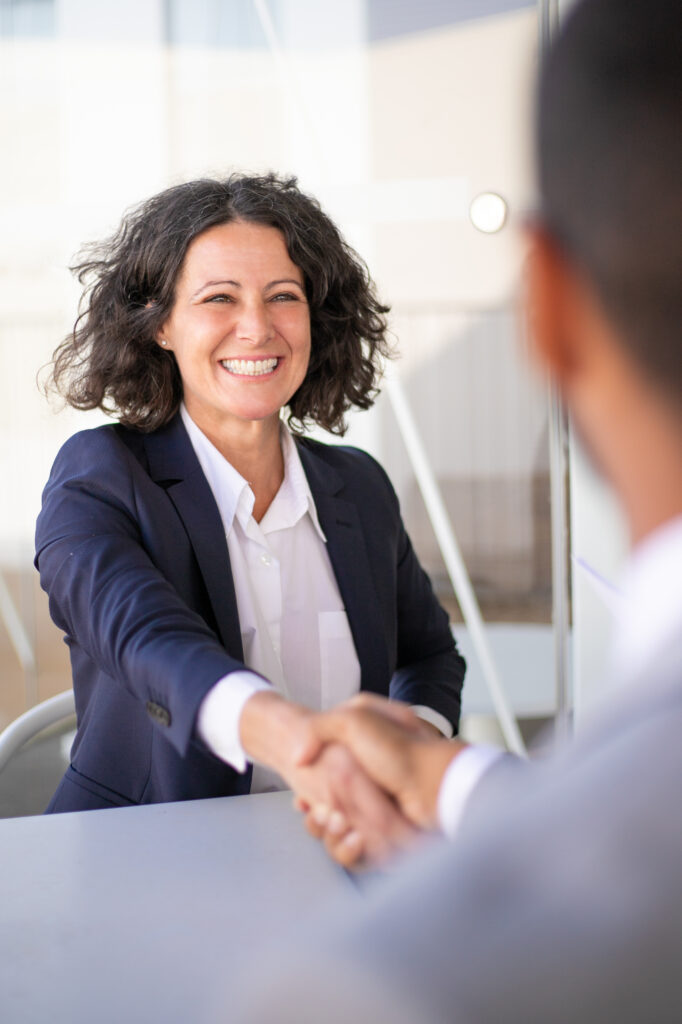 Femme d'affaires souriante en veste bleu marine serrant la main d'un interlocuteur lors d'une rencontre professionnelle en extérieur