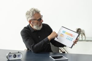older man home showing graph notepad with tablet desk
